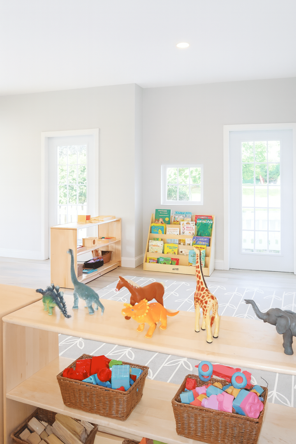 A bright, spacious early childhood classroom at Karter Little Wins, filled with natural light and organized wooden shelves displaying learning materials and sensory toys.