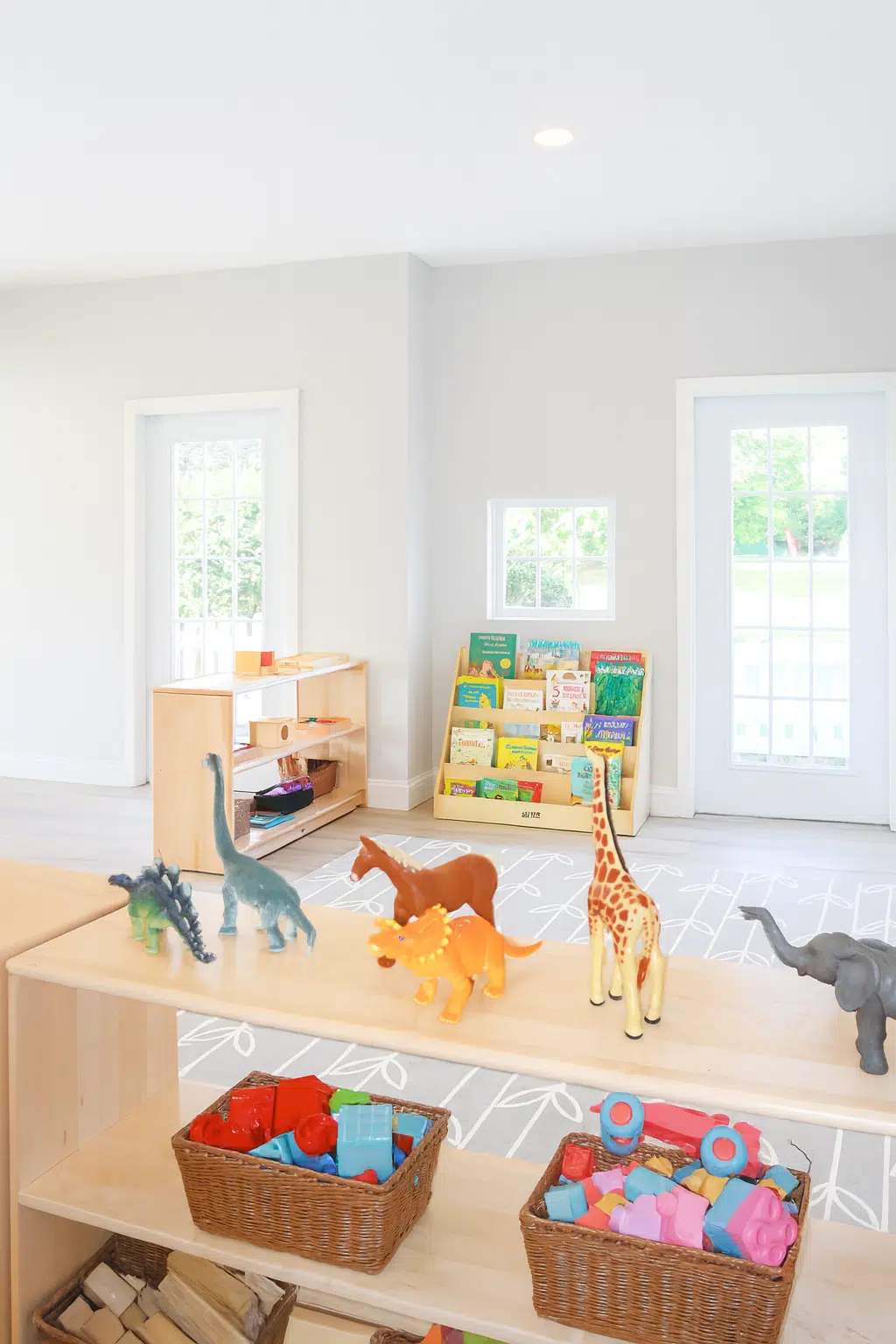 A bright, spacious early childhood classroom at Karter Little Wins, filled with natural light and organized wooden shelves displaying learning materials and sensory toys.